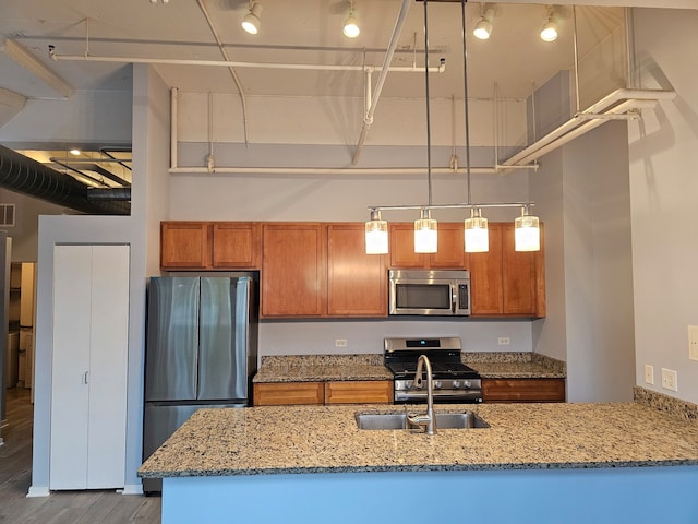 kitchen featuring sink, hanging light fixtures, hardwood / wood-style flooring, light stone countertops, and stainless steel appliances