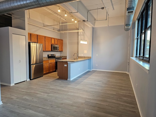 kitchen featuring kitchen peninsula, a towering ceiling, stainless steel appliances, pendant lighting, and light hardwood / wood-style flooring