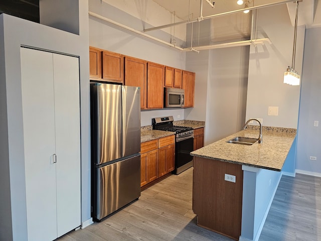 kitchen featuring sink, light wood-type flooring, light stone countertops, appliances with stainless steel finishes, and kitchen peninsula