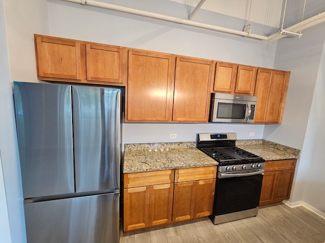 kitchen with light hardwood / wood-style floors, light stone countertops, and stainless steel appliances