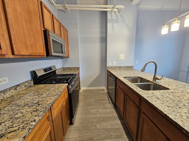 kitchen with hanging light fixtures, sink, appliances with stainless steel finishes, light hardwood / wood-style floors, and light stone counters