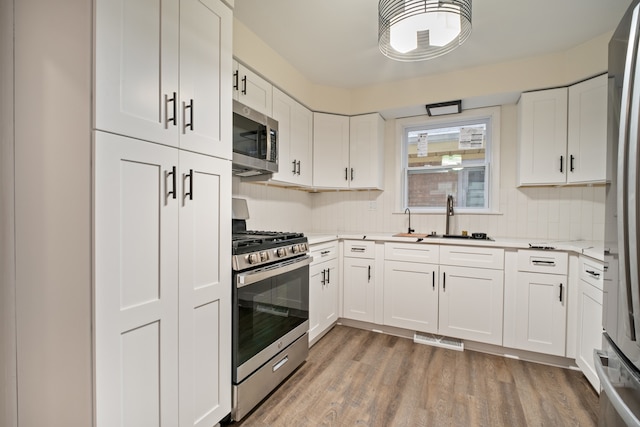 kitchen featuring sink, stainless steel appliances, backsplash, light hardwood / wood-style floors, and white cabinets