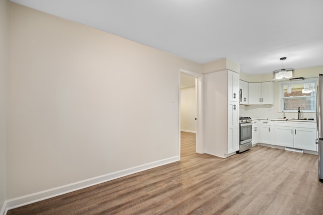 kitchen featuring white cabinetry, stainless steel gas stove, hanging light fixtures, and light hardwood / wood-style flooring