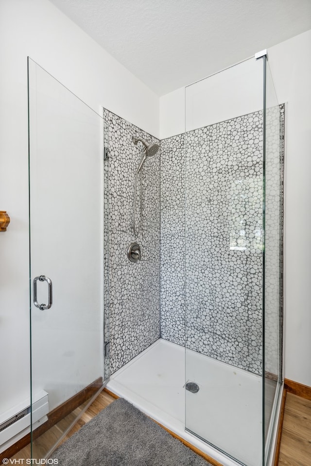 bathroom featuring wood-type flooring, a shower with shower door, and a baseboard heating unit