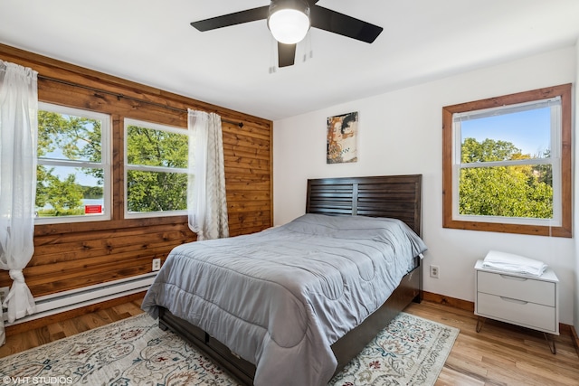 bedroom with multiple windows, light hardwood / wood-style flooring, ceiling fan, and wood walls