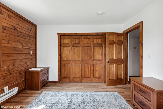 bedroom with wood walls, light wood-type flooring, and baseboard heating