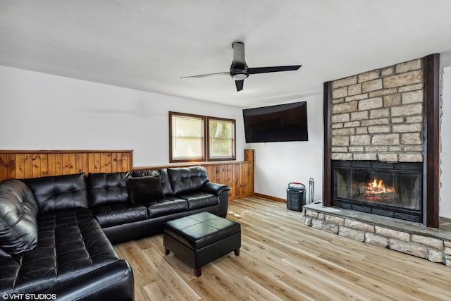 living room with light hardwood / wood-style floors, a stone fireplace, and ceiling fan