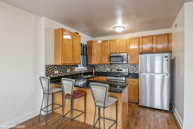 kitchen with kitchen peninsula, appliances with stainless steel finishes, dark wood-type flooring, and a kitchen breakfast bar