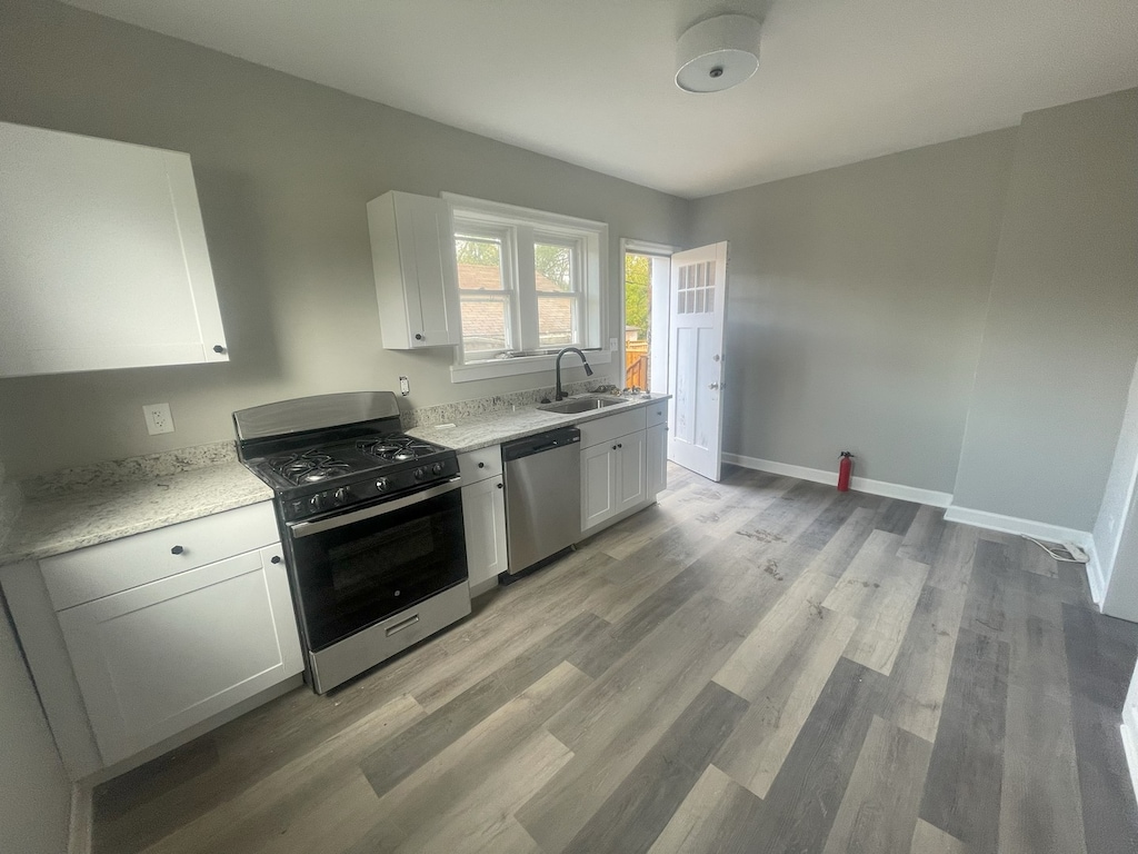 kitchen with light stone countertops, appliances with stainless steel finishes, sink, light hardwood / wood-style flooring, and white cabinets