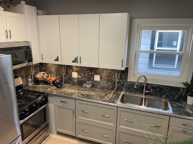 kitchen with appliances with stainless steel finishes, backsplash, sink, dark stone countertops, and white cabinets