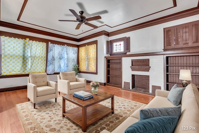 living room featuring a fireplace, crown molding, light hardwood / wood-style flooring, and ceiling fan