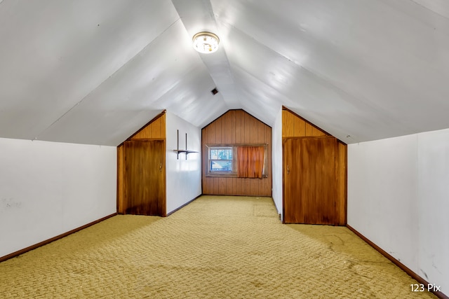 bonus room with light carpet, lofted ceiling, and wood walls