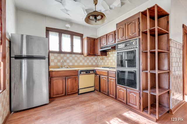 kitchen with sink, stainless steel appliances, range hood, decorative backsplash, and light wood-type flooring