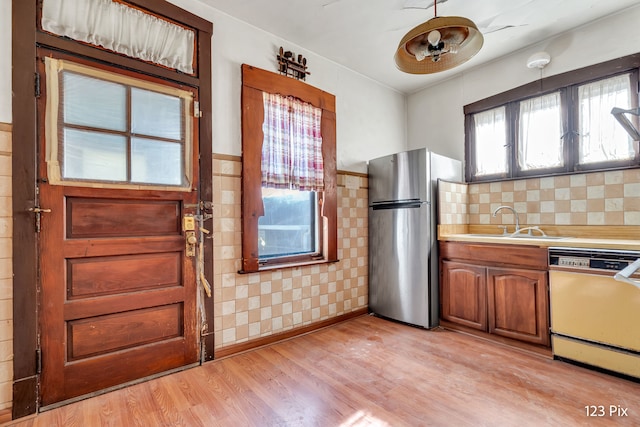 kitchen with dishwasher, sink, stainless steel fridge, light hardwood / wood-style floors, and tile walls