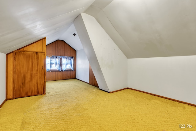 bonus room featuring light carpet, wooden walls, and vaulted ceiling