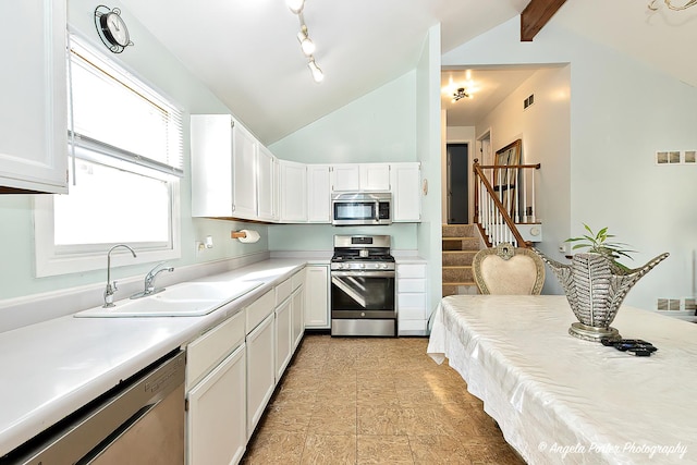 kitchen with white cabinets, vaulted ceiling with beams, stainless steel appliances, and sink