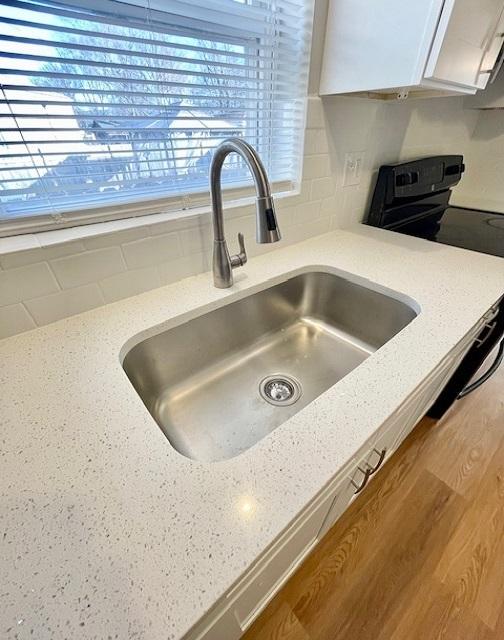 details with white cabinetry, sink, light stone counters, and black / electric stove