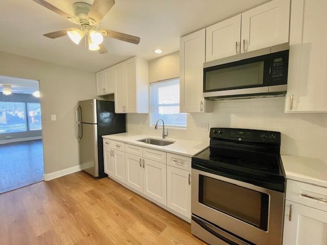 kitchen with white cabinetry, sink, backsplash, light hardwood / wood-style floors, and stainless steel appliances