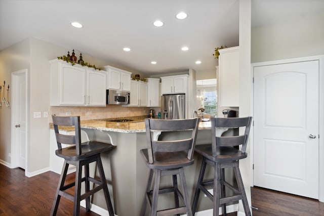 kitchen featuring kitchen peninsula, stainless steel appliances, dark wood-type flooring, white cabinets, and a breakfast bar area