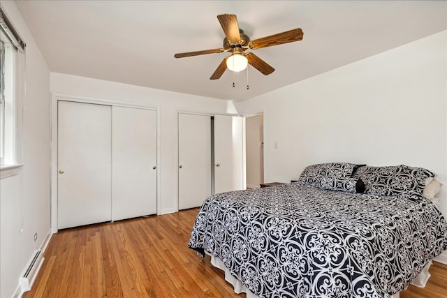 bedroom featuring multiple closets, light hardwood / wood-style flooring, ceiling fan, and a baseboard heating unit