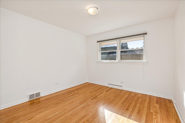 unfurnished room featuring baseboard heating and light hardwood / wood-style floors