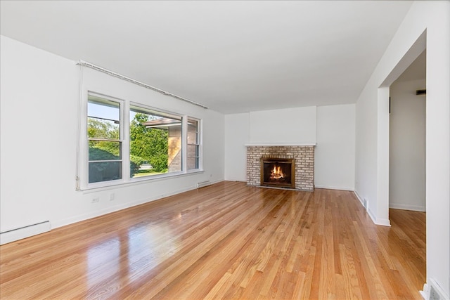 unfurnished living room with baseboard heating, light hardwood / wood-style floors, and a brick fireplace