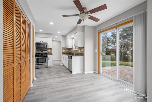 kitchen with light wood-type flooring, tasteful backsplash, stainless steel appliances, ceiling fan, and white cabinets