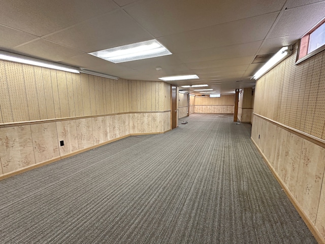 basement featuring a paneled ceiling, dark carpet, and wood walls