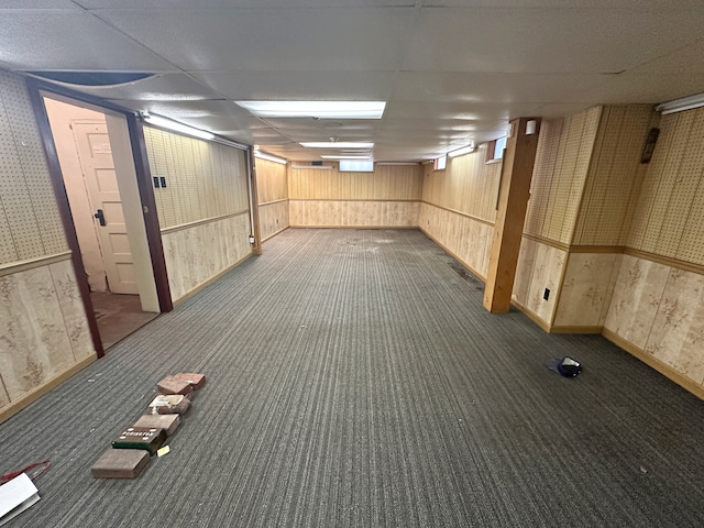 basement with dark colored carpet, a drop ceiling, and wooden walls