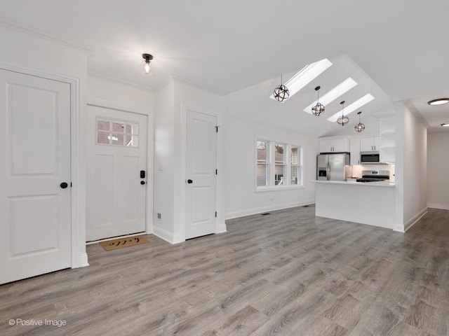 foyer entrance with vaulted ceiling with skylight, ornamental molding, and light wood-type flooring