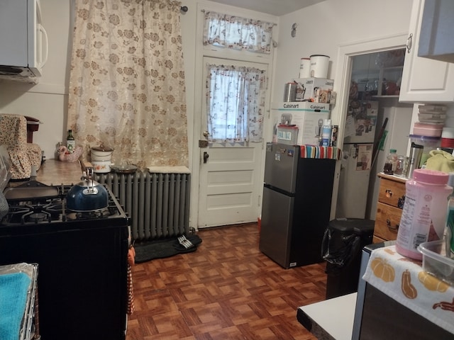 interior space featuring white cabinets, dark parquet floors, radiator heating unit, and stainless steel refrigerator