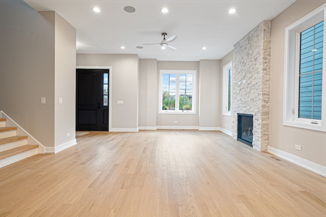 unfurnished living room featuring light hardwood / wood-style floors, a stone fireplace, and ceiling fan