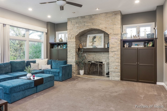 carpeted living room with ceiling fan and a stone fireplace