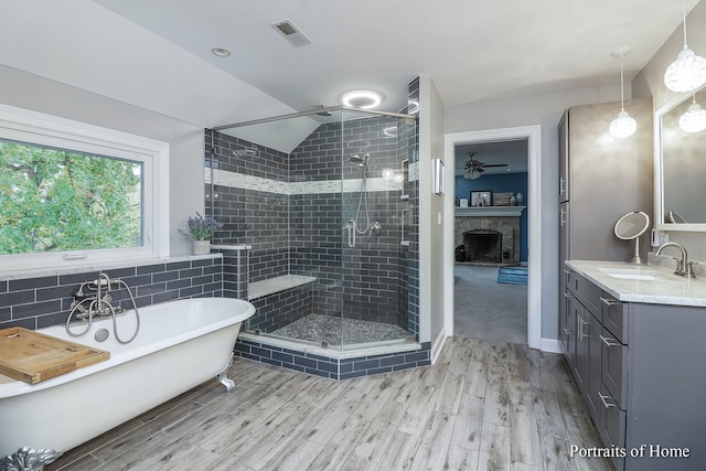 bathroom featuring vanity, lofted ceiling, plus walk in shower, a stone fireplace, and wood-type flooring