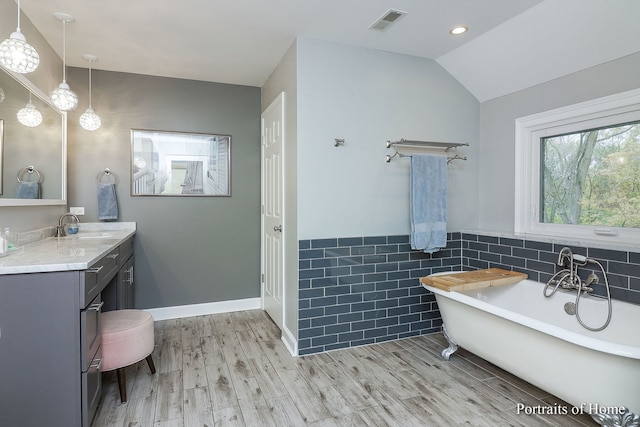 bathroom featuring hardwood / wood-style floors, vanity, lofted ceiling, a bath, and tile walls