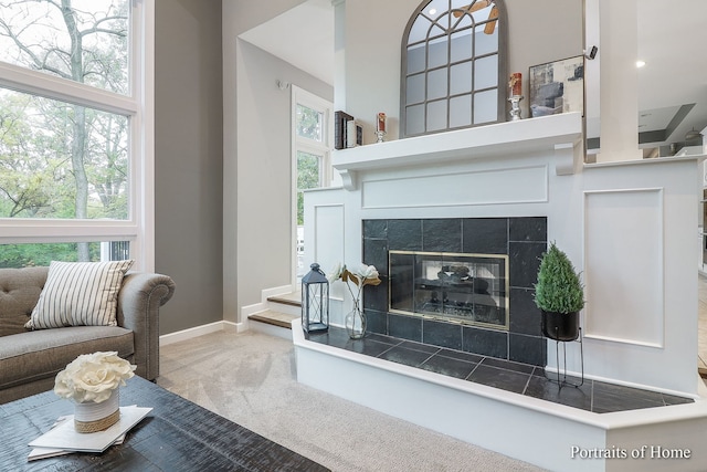 carpeted living room featuring a tile fireplace, a high ceiling, and a wealth of natural light