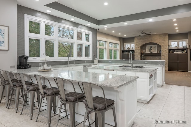 kitchen featuring a breakfast bar, a center island, ceiling fan, light stone counters, and white cabinetry