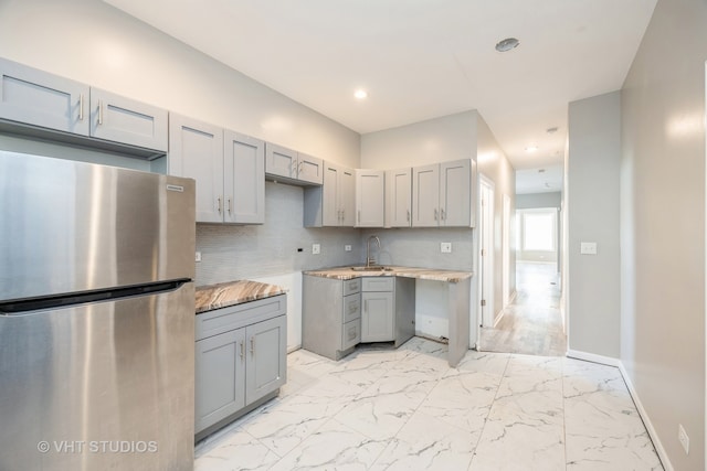 kitchen featuring gray cabinetry, light stone countertops, sink, tasteful backsplash, and stainless steel fridge