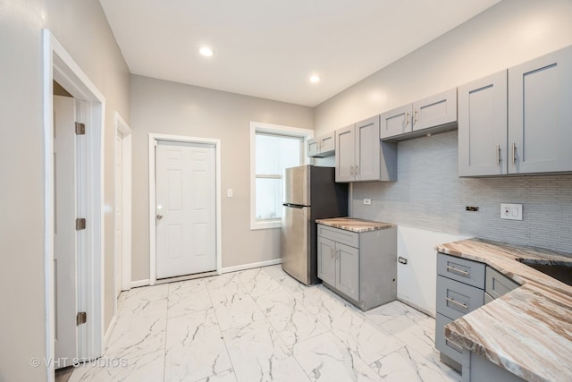 kitchen featuring decorative backsplash, stainless steel fridge, gray cabinets, and butcher block counters