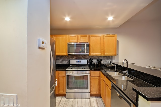 kitchen with sink, decorative backsplash, dark stone countertops, appliances with stainless steel finishes, and kitchen peninsula