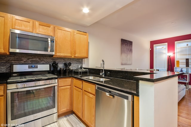 kitchen featuring dark stone counters, sink, light hardwood / wood-style flooring, kitchen peninsula, and stainless steel appliances