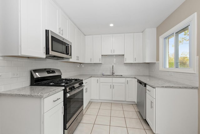 kitchen with appliances with stainless steel finishes, tasteful backsplash, sink, white cabinets, and light tile patterned flooring