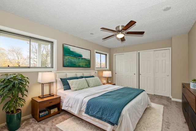 bedroom with two closets, a textured ceiling, light colored carpet, and ceiling fan