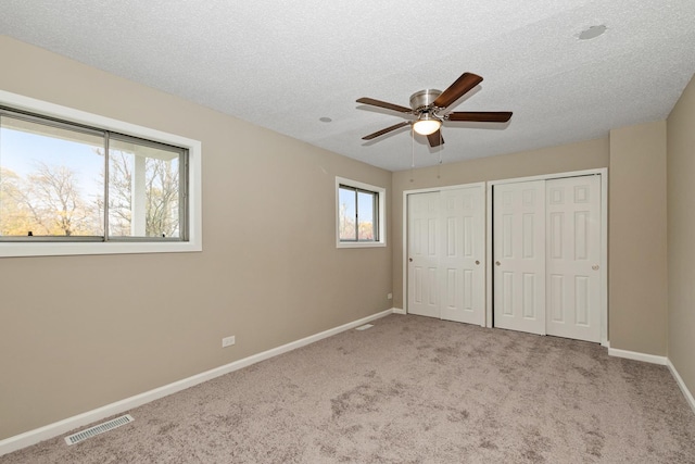 unfurnished bedroom featuring ceiling fan, light colored carpet, and multiple closets