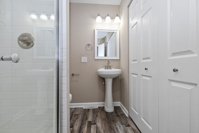 bathroom with toilet, a shower with shower door, and hardwood / wood-style flooring