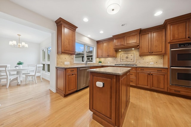 kitchen with light stone counters, decorative light fixtures, light hardwood / wood-style flooring, appliances with stainless steel finishes, and a kitchen island