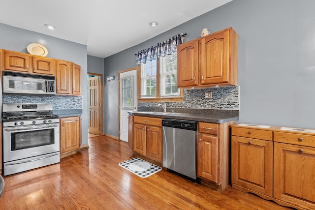 kitchen with decorative backsplash, sink, light wood-type flooring, and appliances with stainless steel finishes