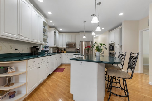 kitchen with pendant lighting, white cabinets, a kitchen breakfast bar, light hardwood / wood-style flooring, and stainless steel appliances