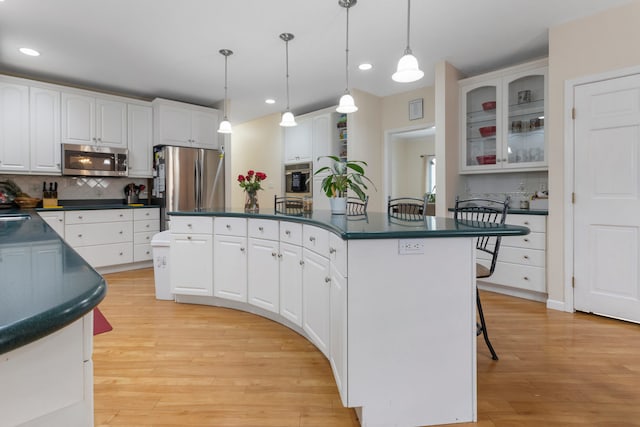 kitchen featuring appliances with stainless steel finishes, backsplash, white cabinets, a center island, and hanging light fixtures