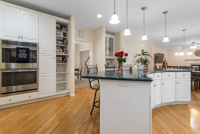 kitchen featuring white cabinets, a kitchen breakfast bar, hanging light fixtures, and double oven